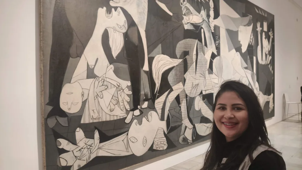 Mulher sorrindo em frente ao famoso quadro "Guernica" de Pablo Picasso, em exibição em um museu